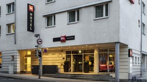 A hotel with a modern facade, a prominent 'ibis' sign, and a ground-level entrance with a glass door. - ibis Stuttgart Centrum (Stuttgart)
