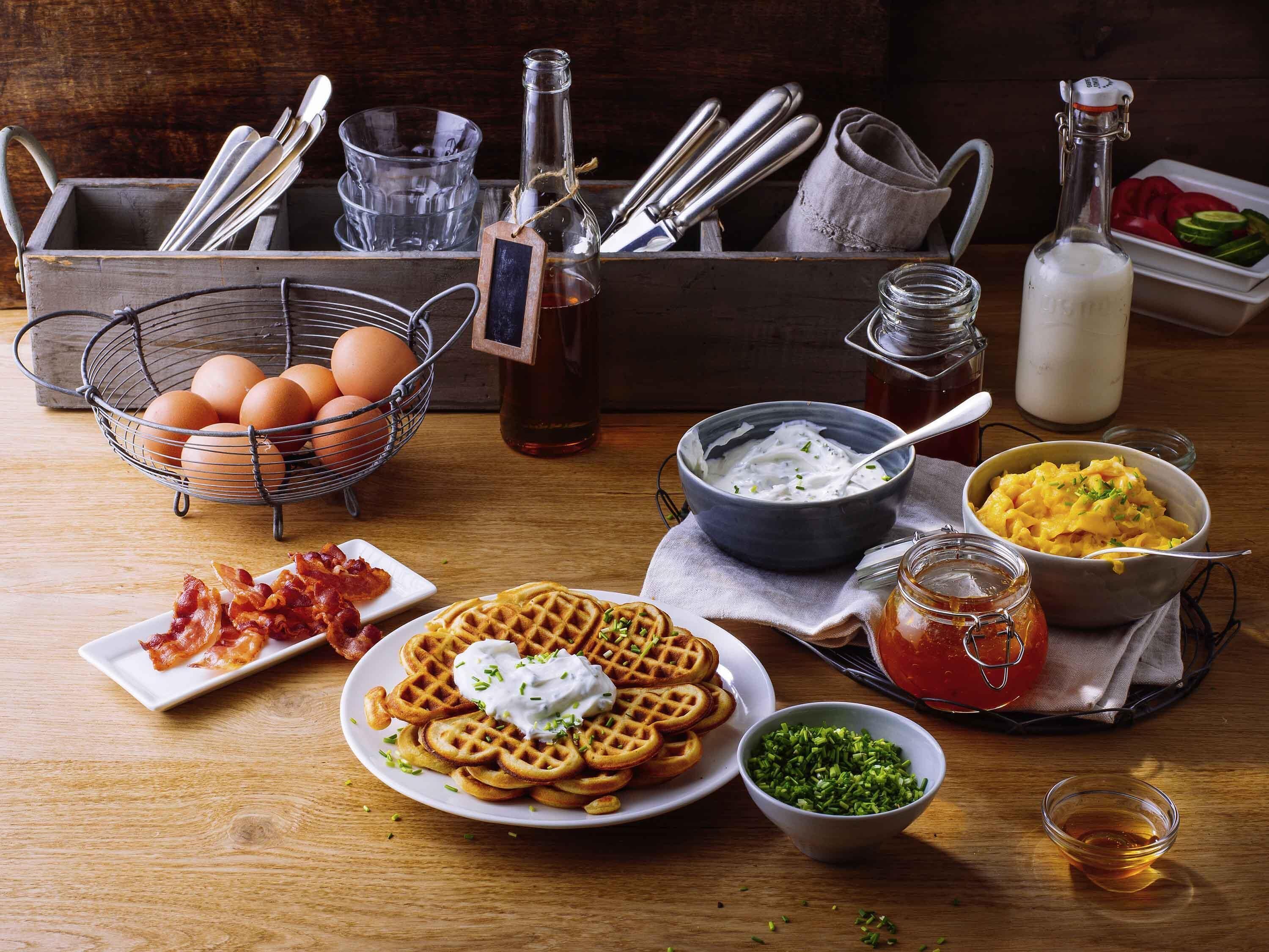 A breakfast setting with waffles, eggs, bacon, yogurt, and condiments.