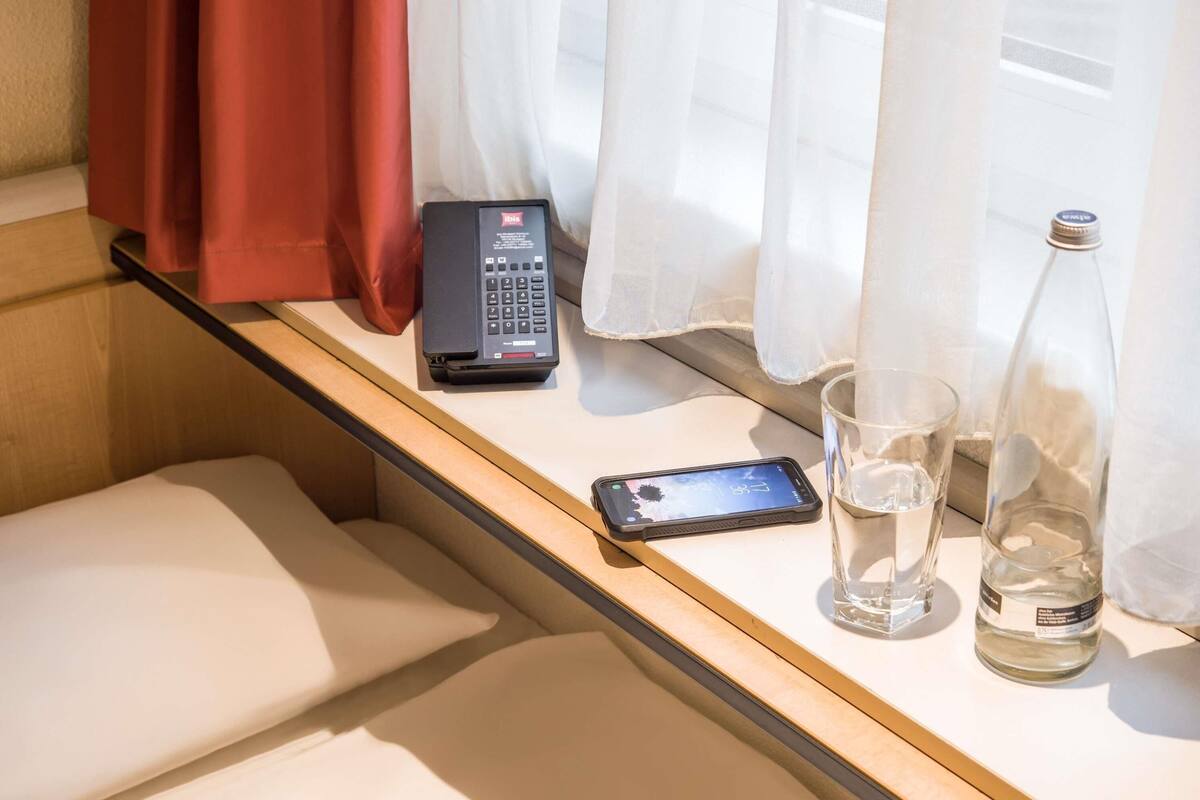 A window seat with a phone, a glass of water, and a bottle on a table.