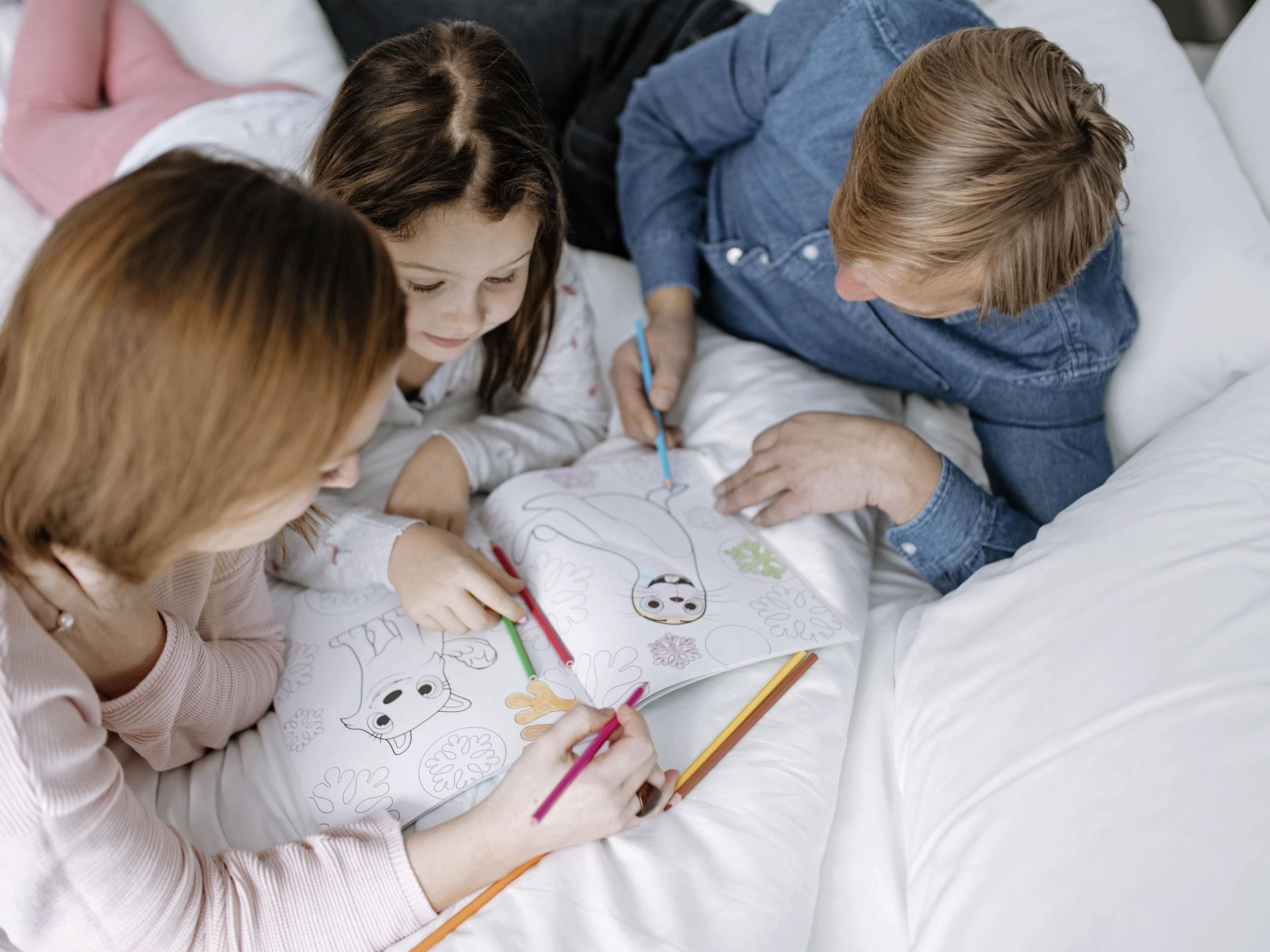 Three people lying on a bed, coloring a book together.