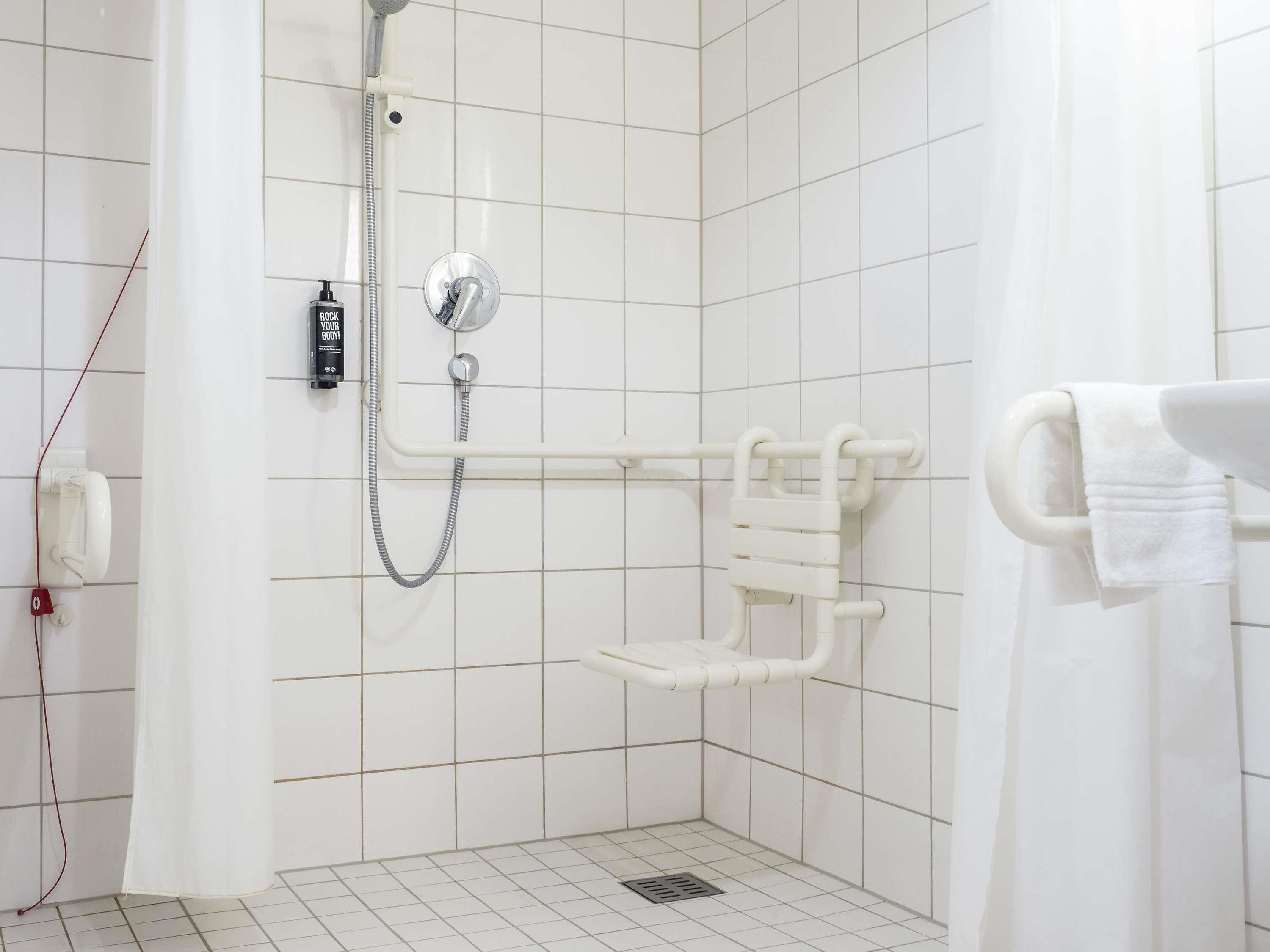 A small, white-tiled shower area with a handheld showerhead, a handheld shower attachment, and a white towel rack.