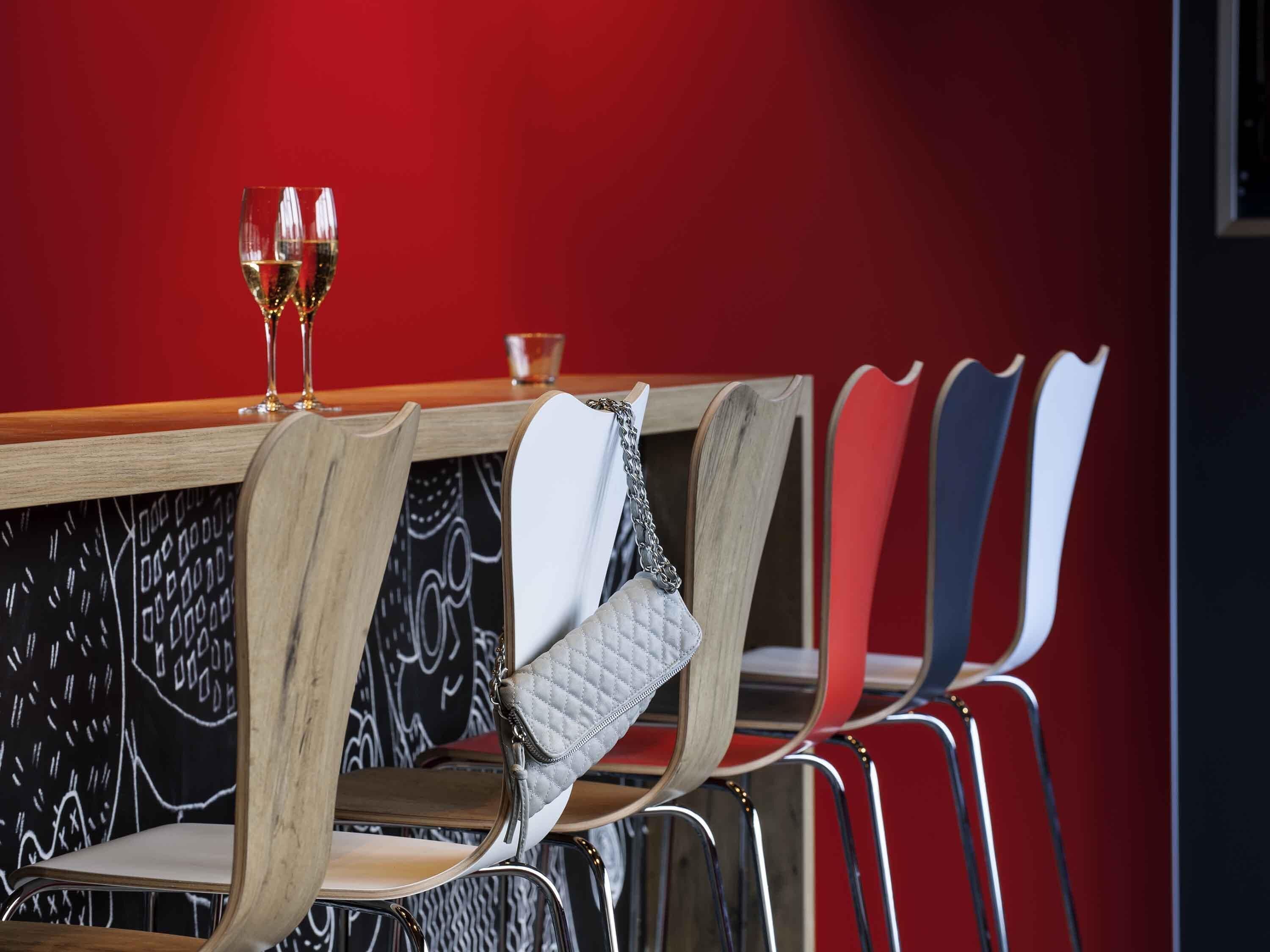 A dining area with a red wall, a wooden table, and chairs with quilted and plain cushions.