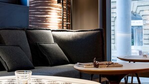 A cozy seating area with a sofa and a round table, featuring a patterned table runner and a glass of water. - ibis Stuttgart Centrum (Stuttgart)
