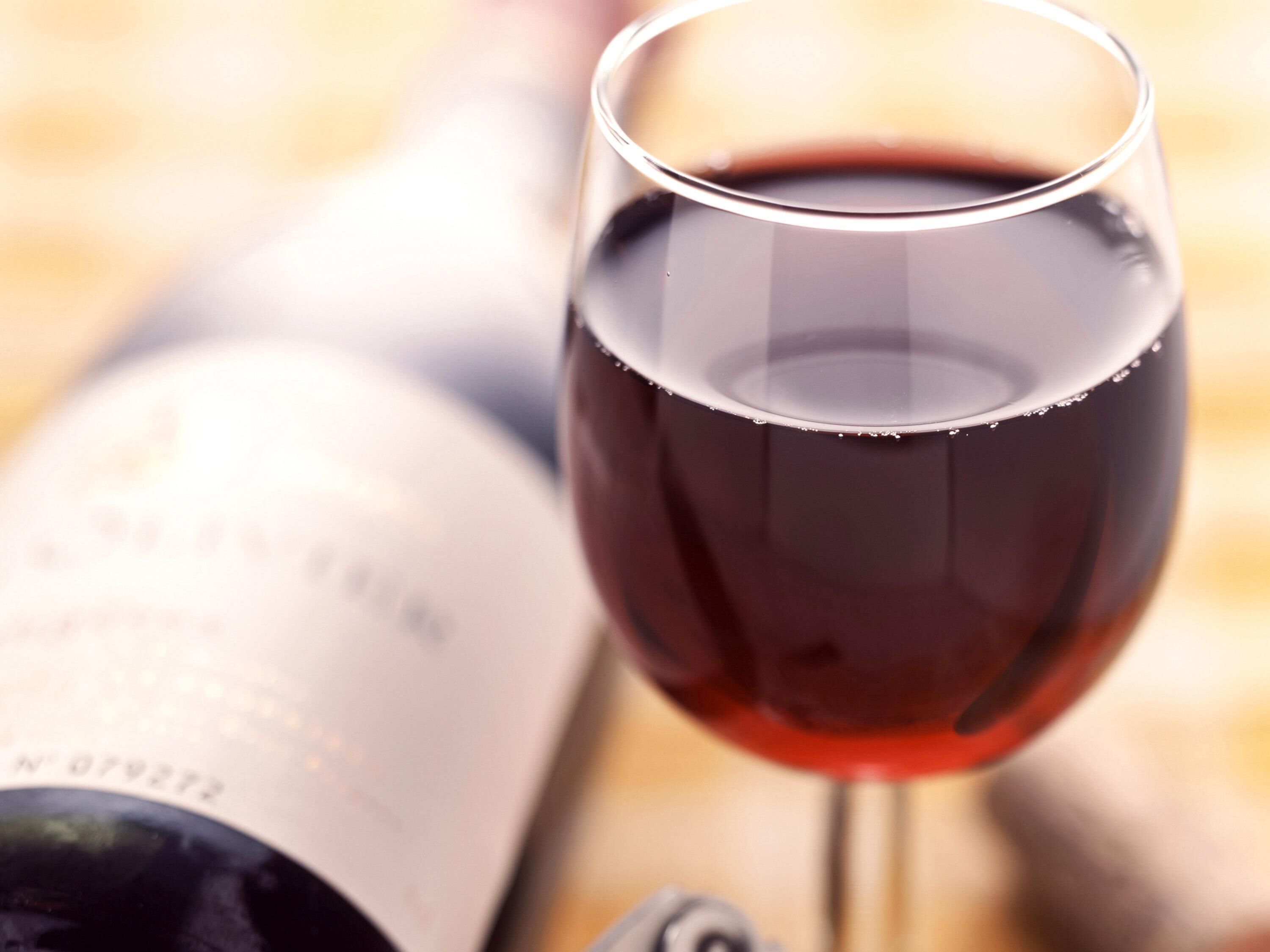 A wine glass filled with red wine, a wine bottle, and a book.