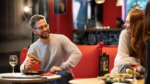 A person sitting on a red couch with a plate of food and a glass of wine on a small round table. - ibis Stuttgart Centrum (Stuttgart)