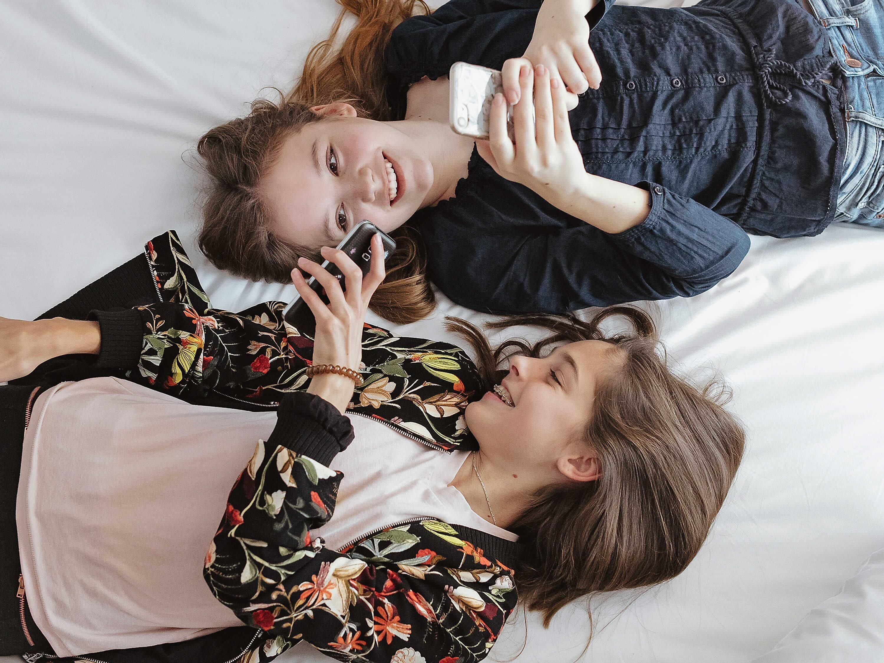 Dos personas acostadas en una cama, una sosteniendo un teléfono inteligente.