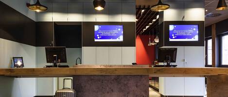A reception desk with a monitor, a red handbag, and a suitcase.