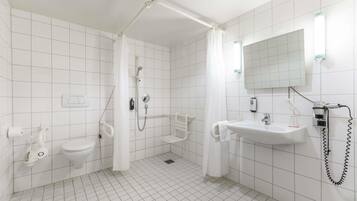 A bathroom with white tiles, a shower, a toilet, a sink, and a mirror.