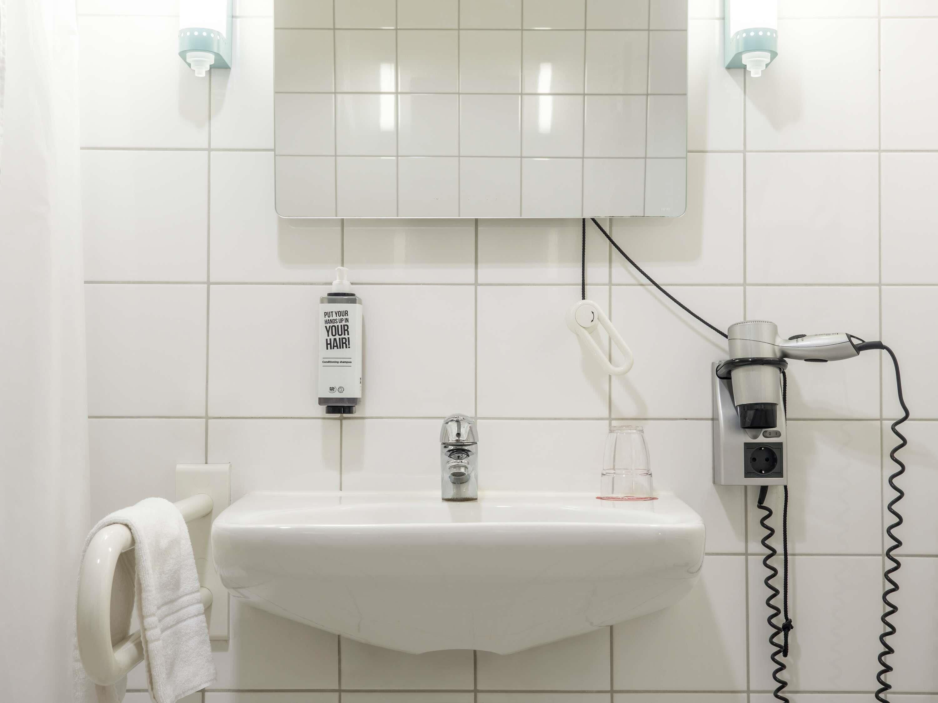A bathroom with a white sink, a towel rack, a hairdryer, and a bottle of shampoo.