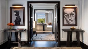 A hallway with framed artwork on either side, leading to a room with a view of greenery. - The Ritz-Carlton New York, Central Park (New York)