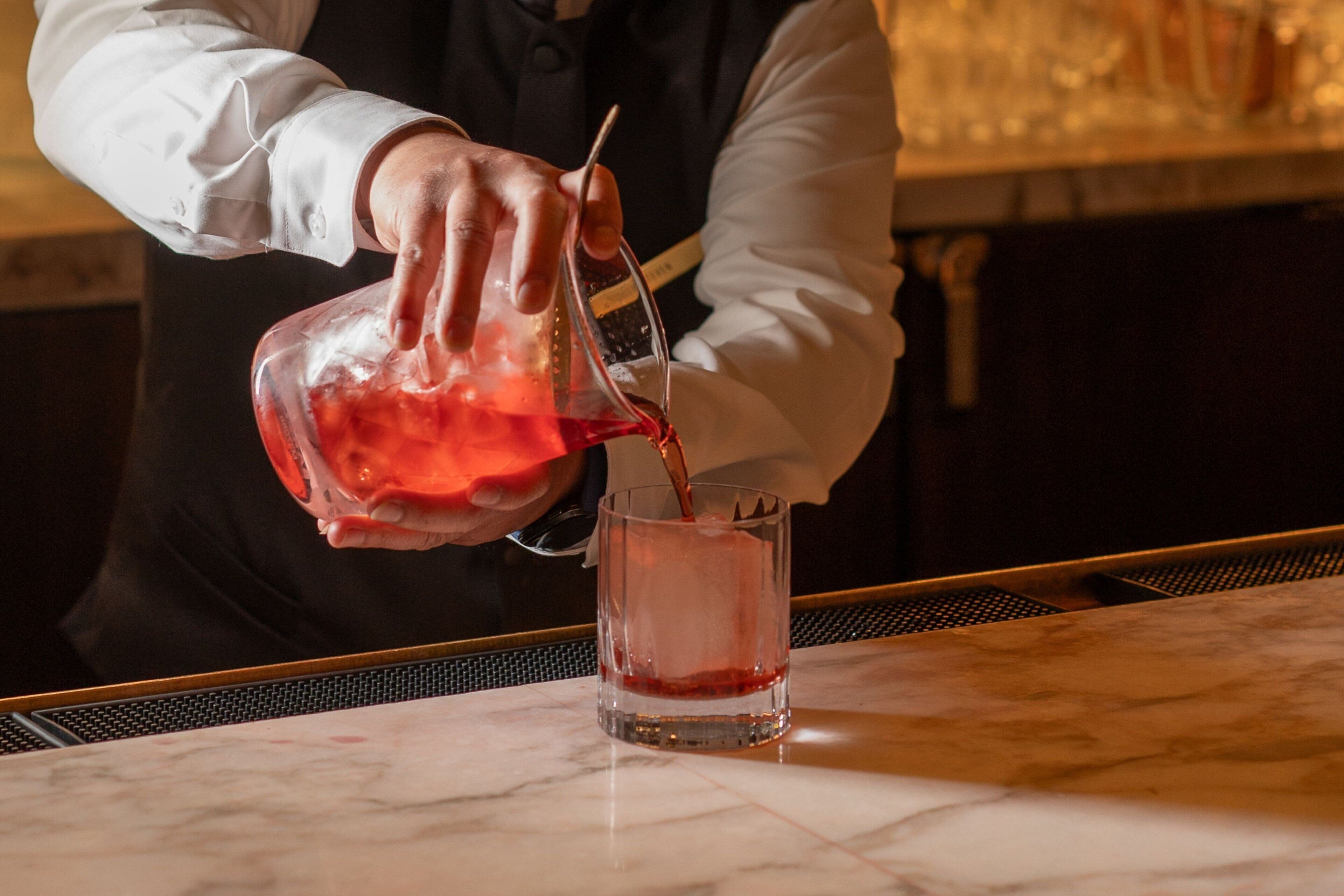 A person pouring a red liquid into a clear glass.
