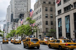 A busy city street with multiple yellow taxis and American flags. - The Ritz-Carlton New York, Central Park (New York)