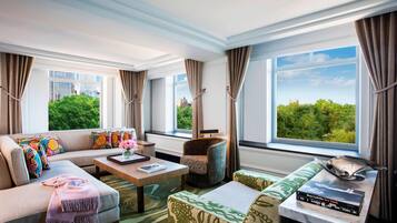 A modern hotel room with a large window, a sofa, a chair, a coffee table, and a small table with books.