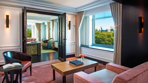 A modern hotel room with a large window, a sofa, a chair, a table with a book, and a vase with a flower. - The Ritz-Carlton New York, Central Park (New York)