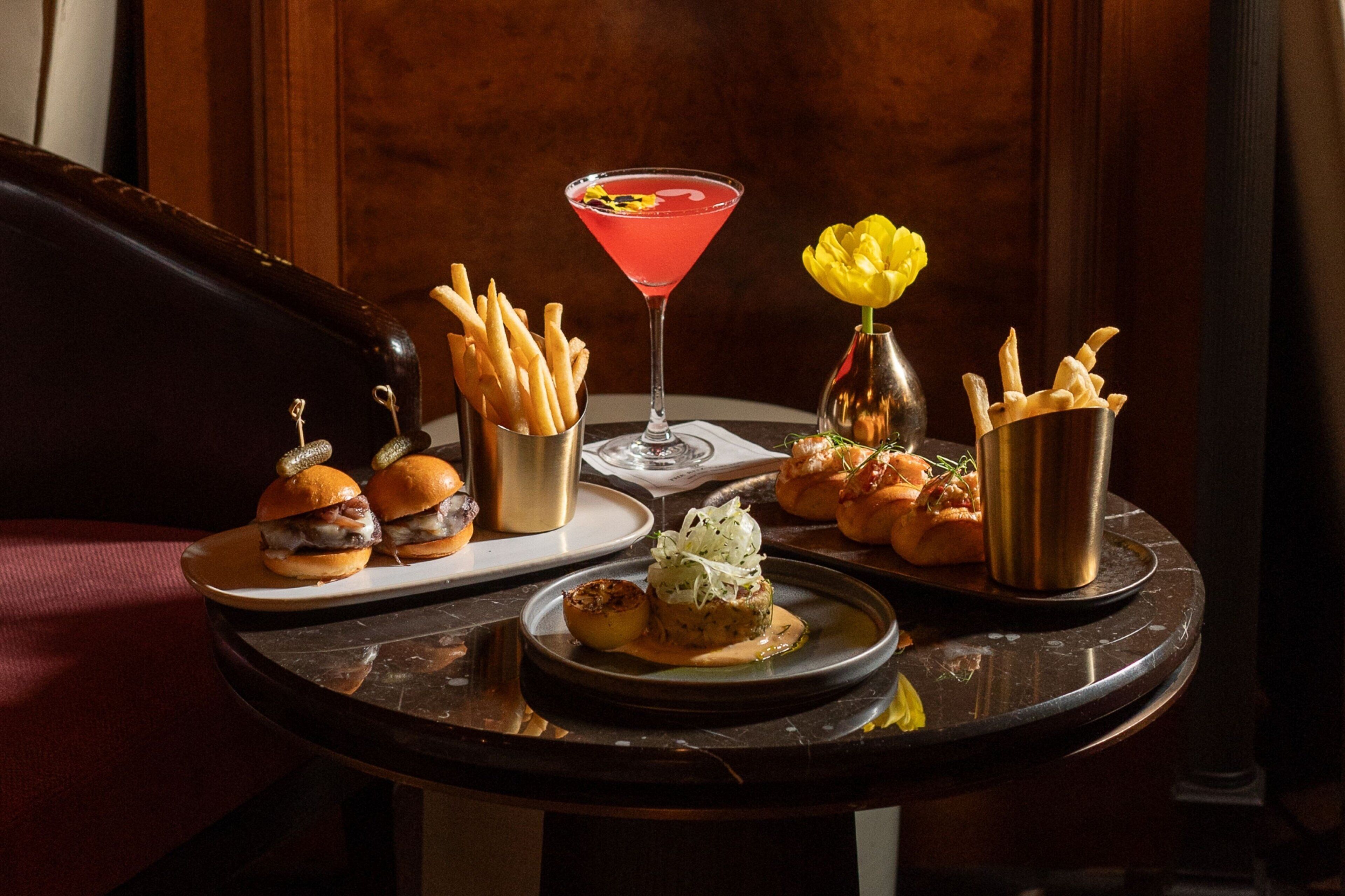 A table with food items including burgers, fries, a martini, and a dessert.