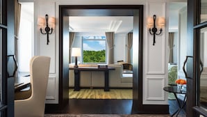 A hotel room with a view of greenery through a window, a sofa, a table, and a chair. - The Ritz-Carlton New York, Central Park (New York)
