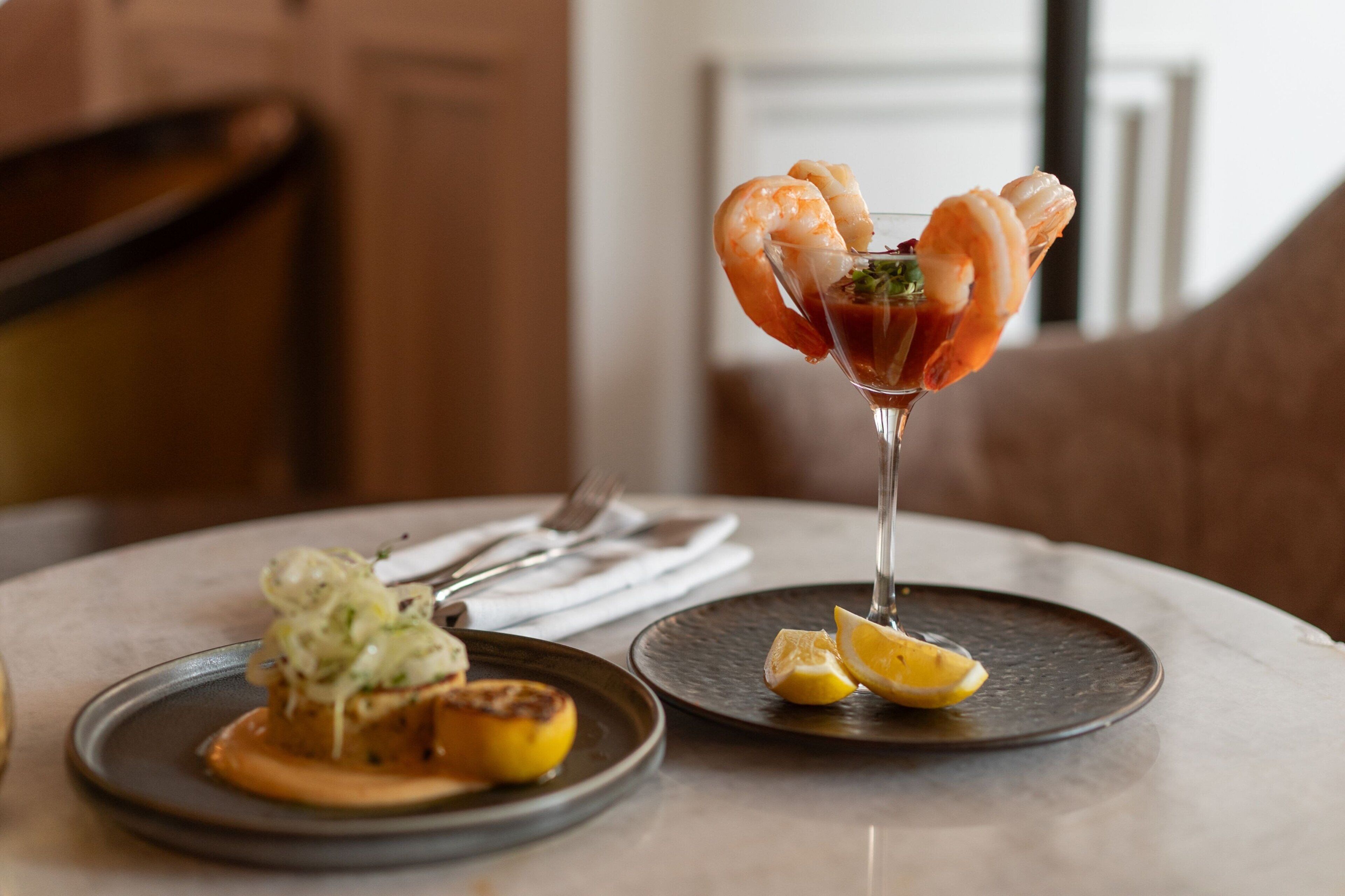 A dining table with a plate of food and a cocktail glass with a shrimp garnish.