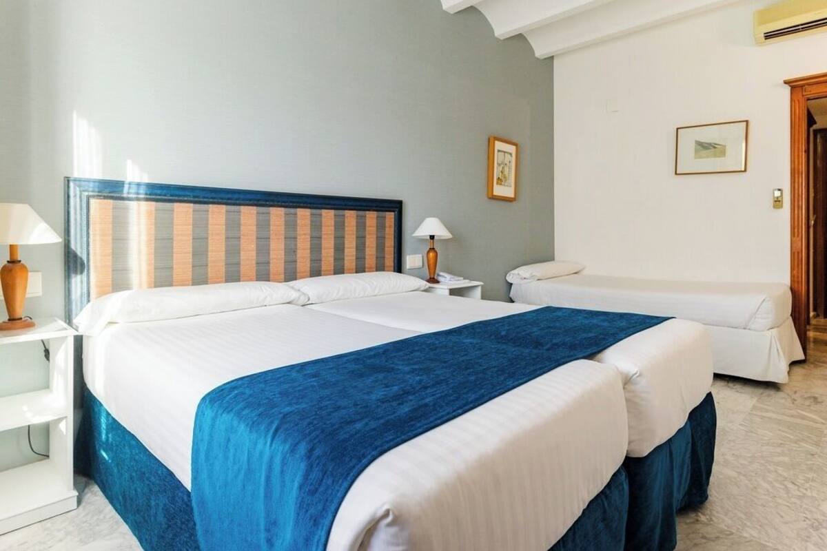 A hotel room with a large bed, a smaller bed, a nightstand, a lamp, and a picture on the wall.