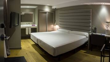 Una habitación de hotel moderna con una cama grande, una mesita de noche, un escritorio, una silla, un espejo, un lavabo y un armario.