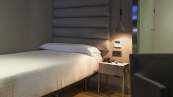 Un dormitorio moderno con cama, mesita de noche, lámpara y sillón.