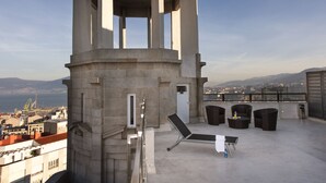 Una terraza en la azotea con vistas a la ciudad y a las montañas, que incluye un área de descanso con sillas y una mesa.