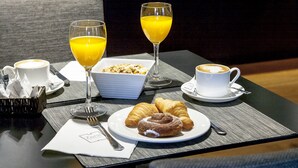Desayuno con croissants, jugo de naranja y café sobre una mesa en una habitación de hotel moderna.
