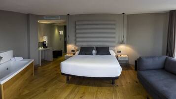 A modern hotel room with a large bed, a sofa, a bathtub, and a city view.
