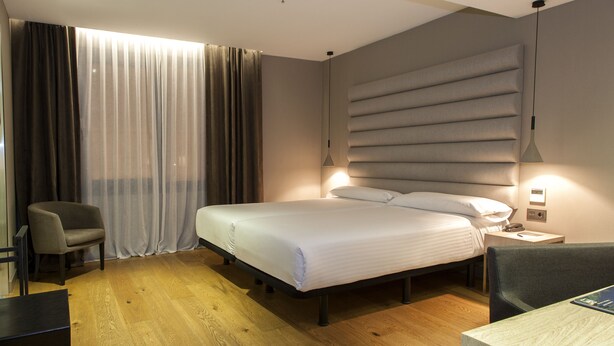 Una habitación de hotel con cama, una silla, un escritorio y una lámpara.