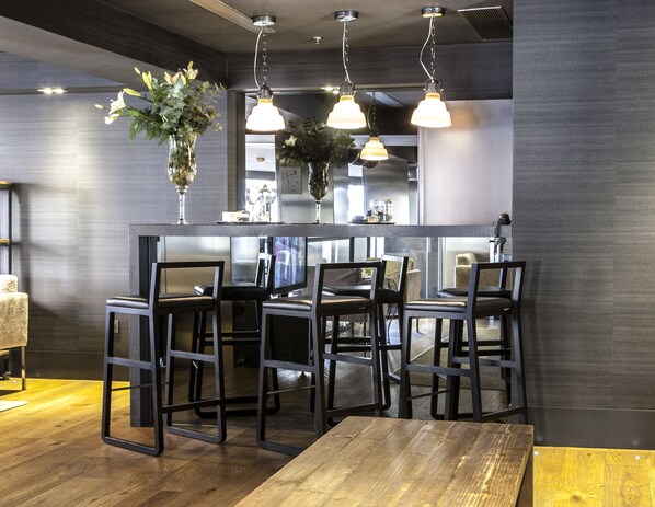 Un espace bar moderne avec un plancher en bois, des chaises en métal noir et des luminaires suspendus.
