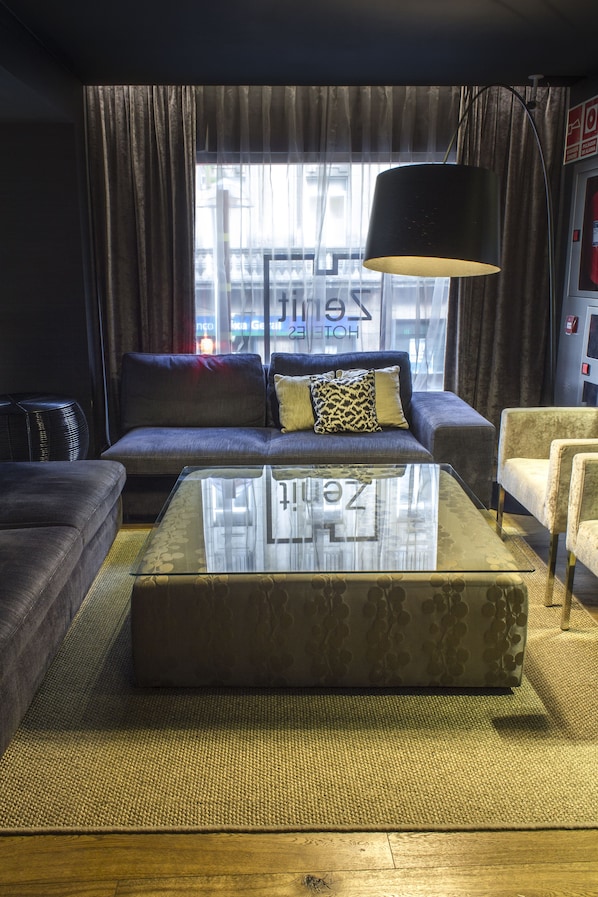 Un salon moderne avec un canapé, des fauteuils, une table basse en verre et une grande fenêtre avec des rideaux.