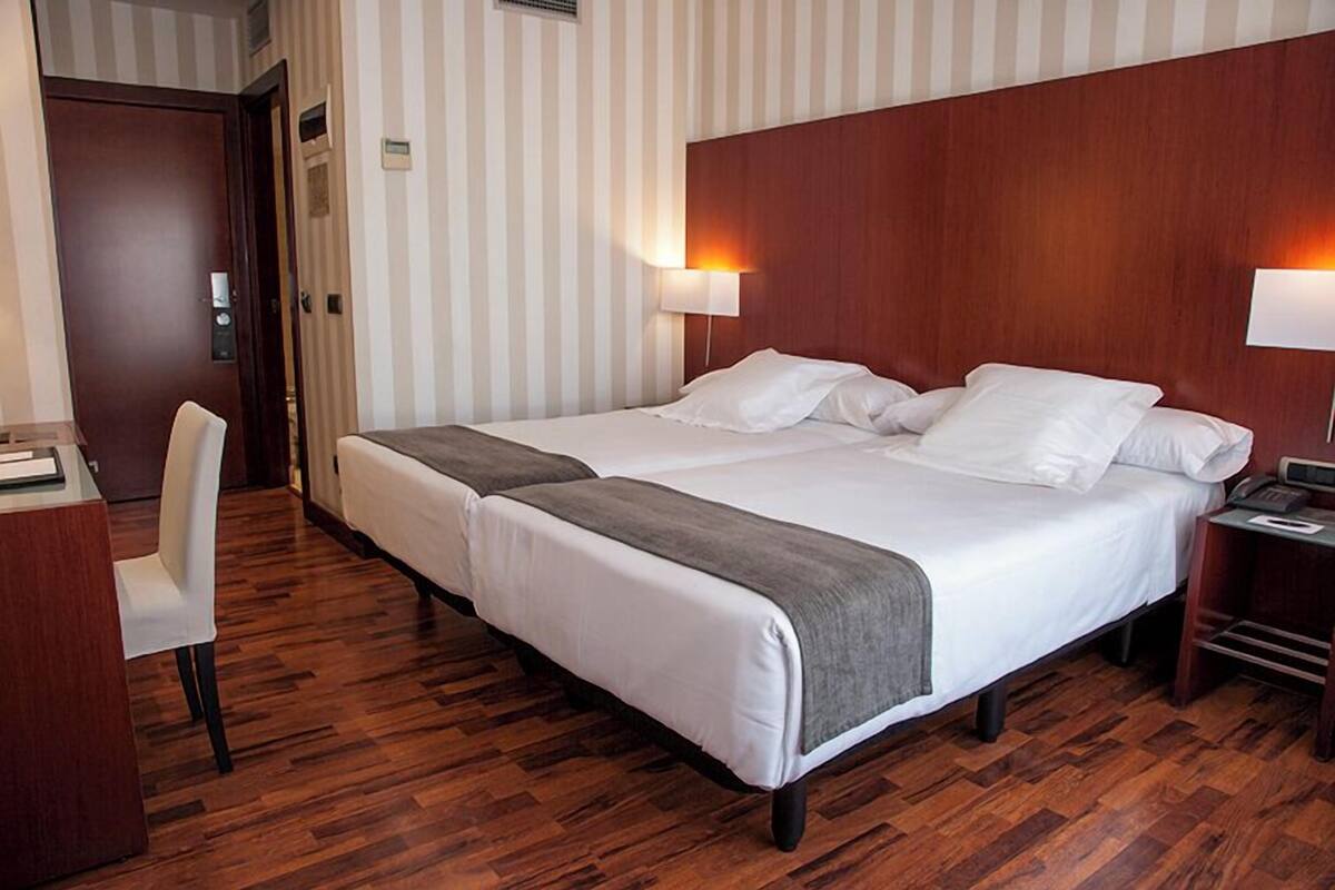 Ein Hotelzimmer mit einem großen Bett, zwei Nachttischen, einem Schreibtisch und einem Stuhl.