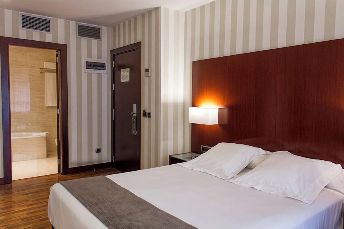 Ein Hotelzimmer mit Bett, Nachttisch, Lampe, einer Tür und einem Schild an der Wand.