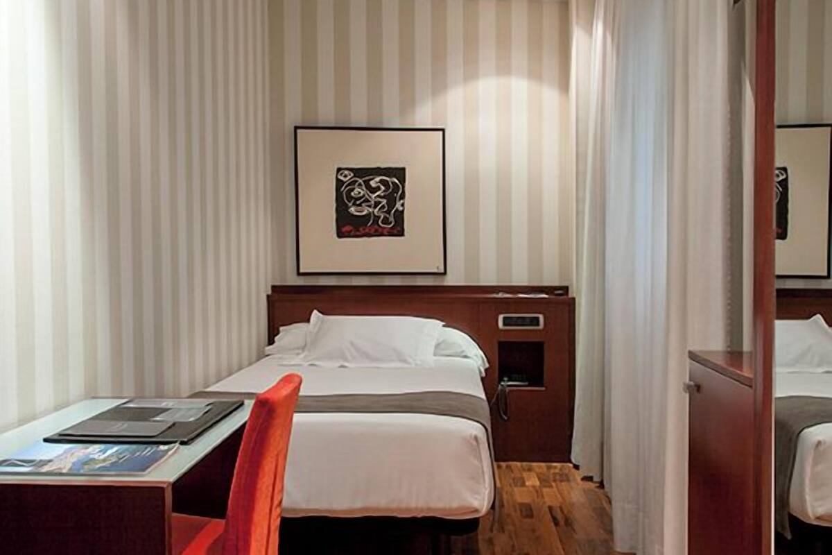 Ein Hotelzimmer mit Bett, Schreibtisch, Stuhl, Flachbildfernseher und einem gerahmten Bild an der Wand.