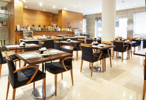Un restaurante moderno con varias mesas y sillas, una zona de bar con diferentes opciones de comida y bebidas, y un interior limpio y bien iluminado.