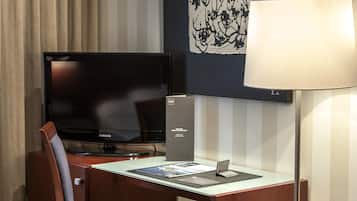 Une chambre d’hôtel avec un lit, un bureau avec un ordinateur, une télévision et une lampe.