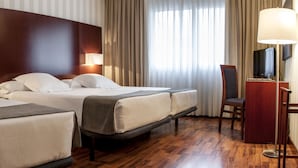 A hotel room with two beds, a desk, a chair, a TV, and a lamp.