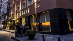 A multi-story hotel with a modern facade, a prominent sign reading "ZENIT HOTELS," and a motorcycle parked outside.