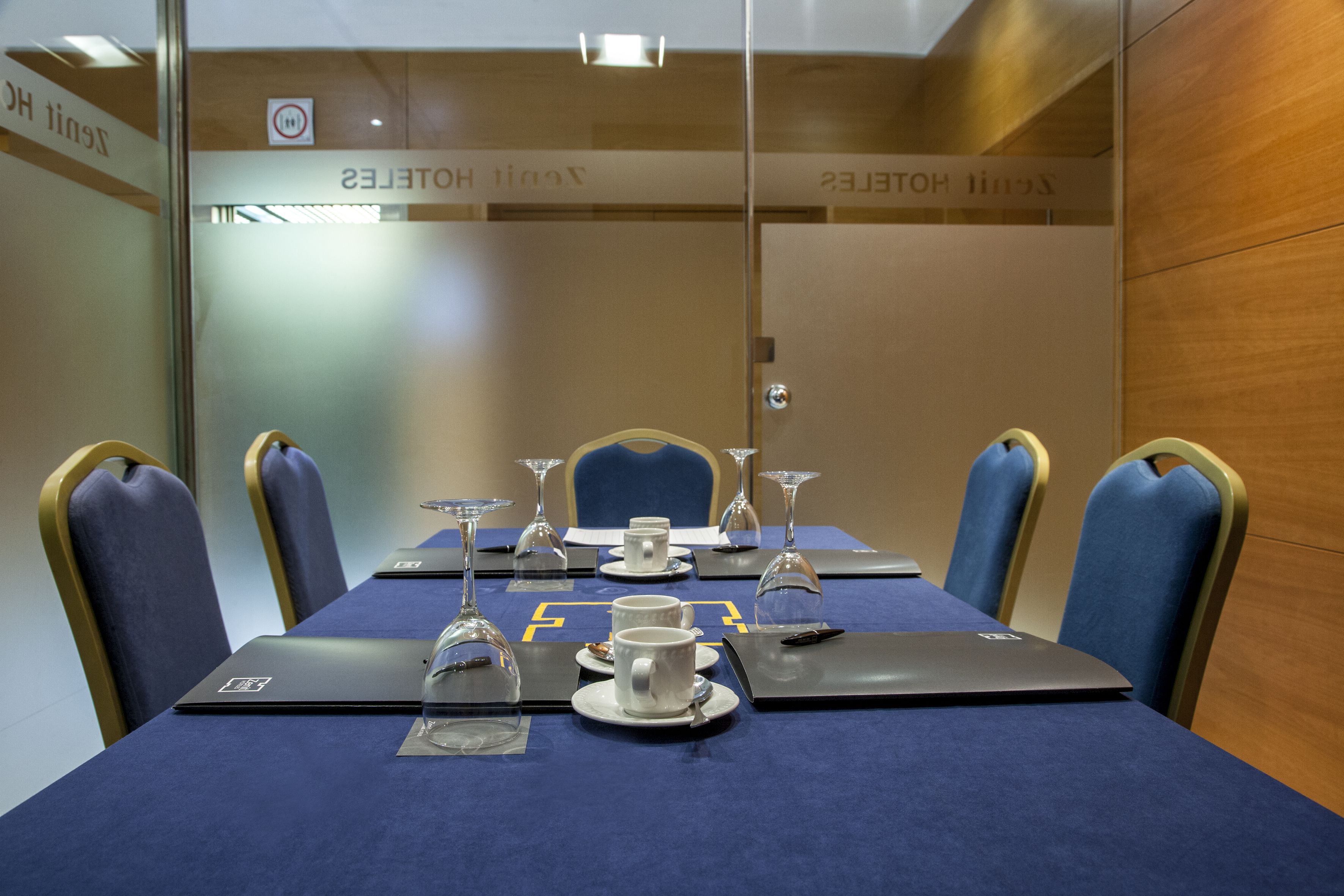 Une salle de conférence avec une table bleue, des tasses blanches et des ordinateurs portables.