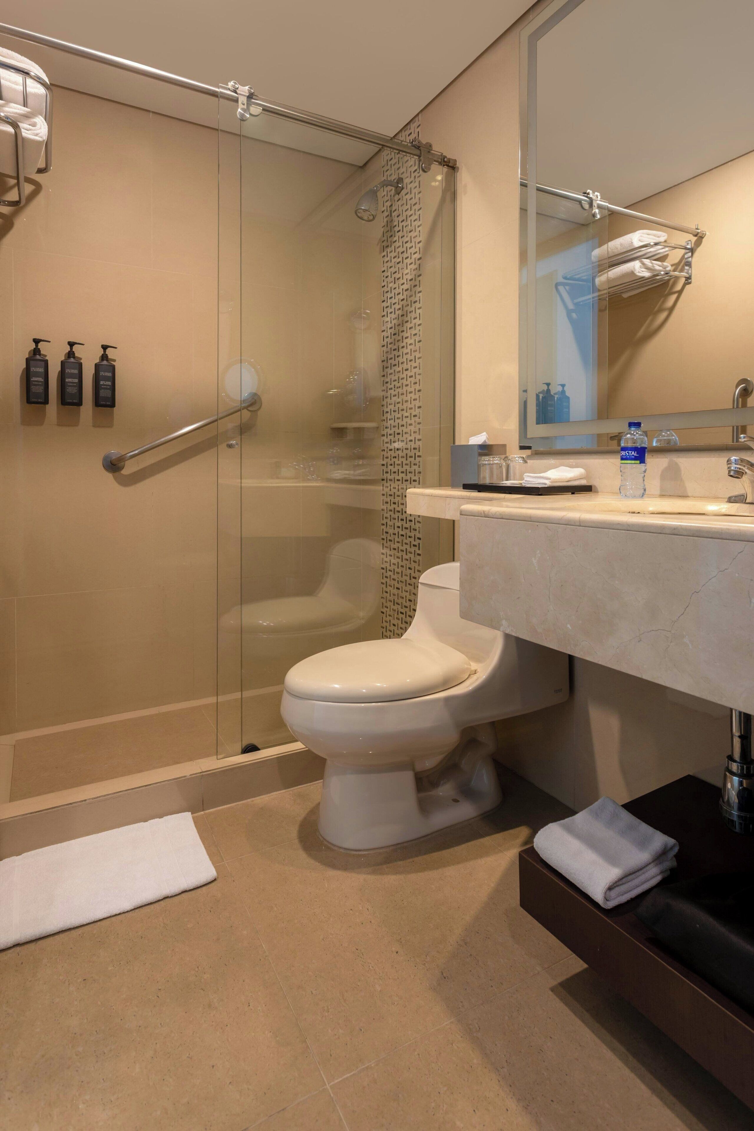 Un baño moderno con cabina de ducha de vidrio, inodoro blanco, lavabo de mármol y un espejo grande.