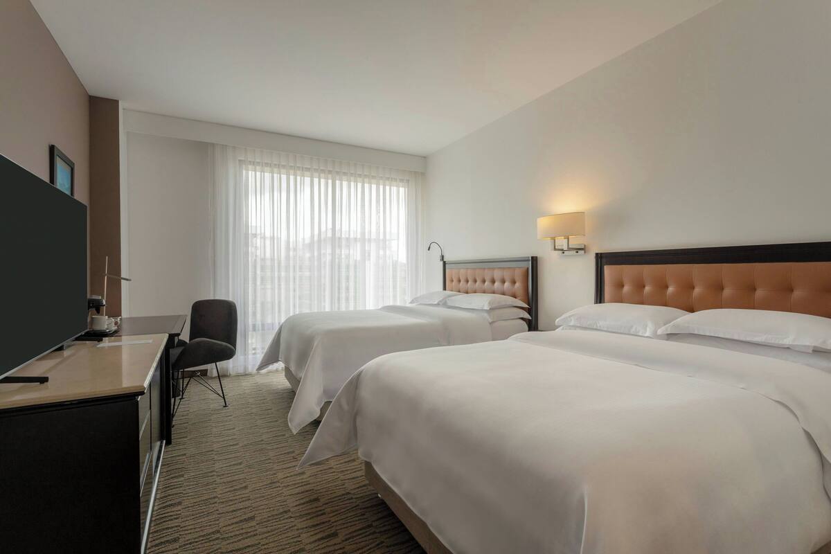 A hotel room with two beds, a desk, a chair, and a TV.