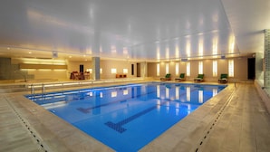An indoor swimming pool with clear lane markings, lounge chairs, and a reception area with a counter and chairs.