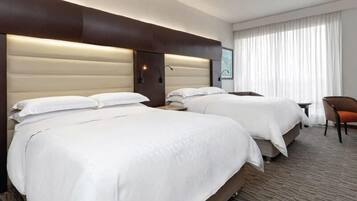 A hotel room with two beds, a chair, and a large window with curtains.