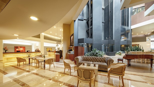 A spacious lobby with a checkered marble floor, a seating area with sofas and chairs, a piano, and a reception desk.