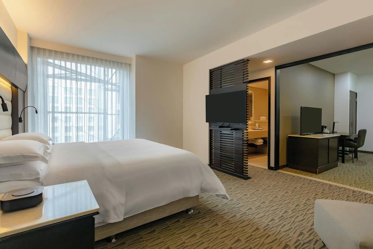 A hotel room with a large bed, a desk with a flat-screen TV, a desk lamp, and a chair.