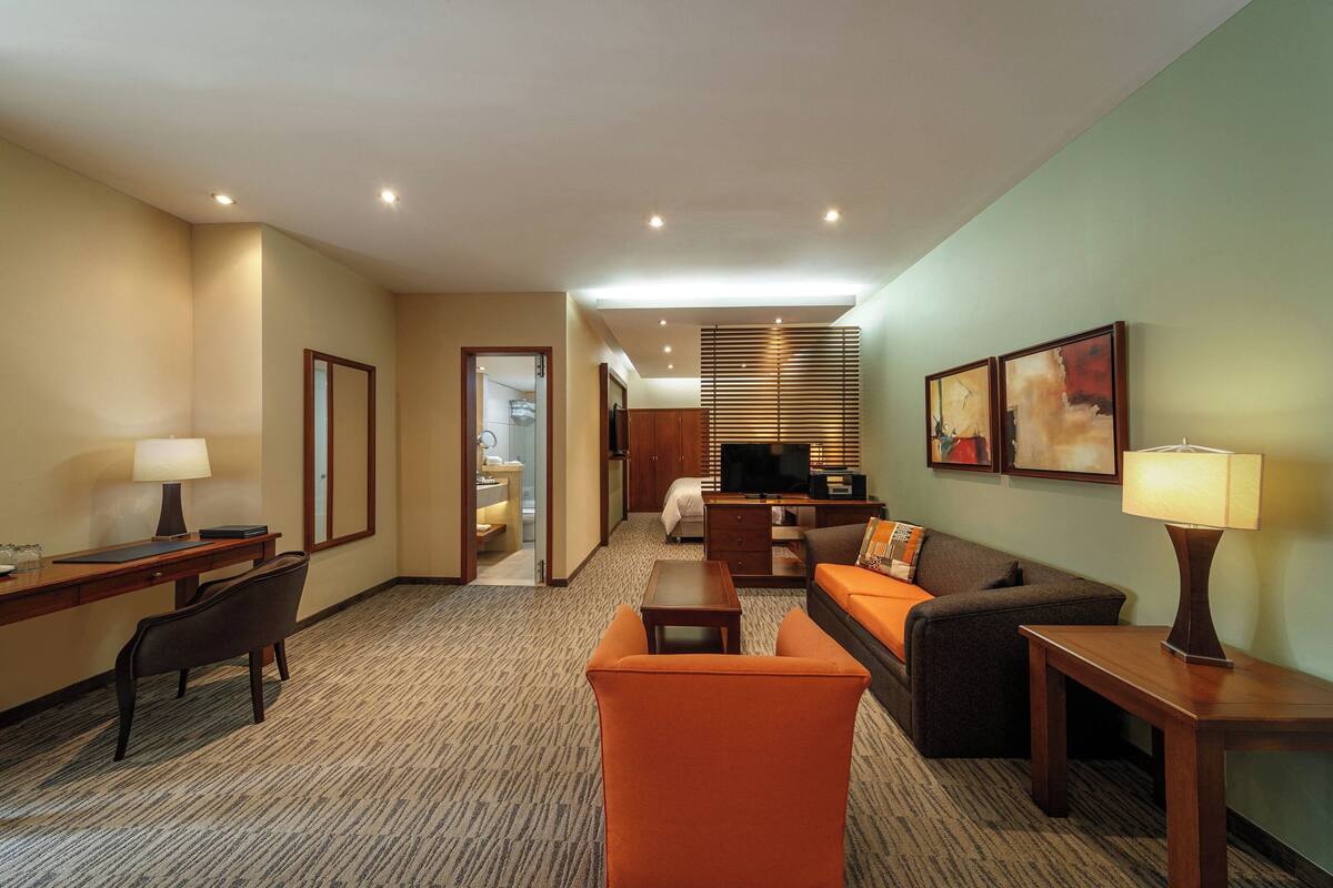 A hotel room with a desk, chair, sofa, and television.