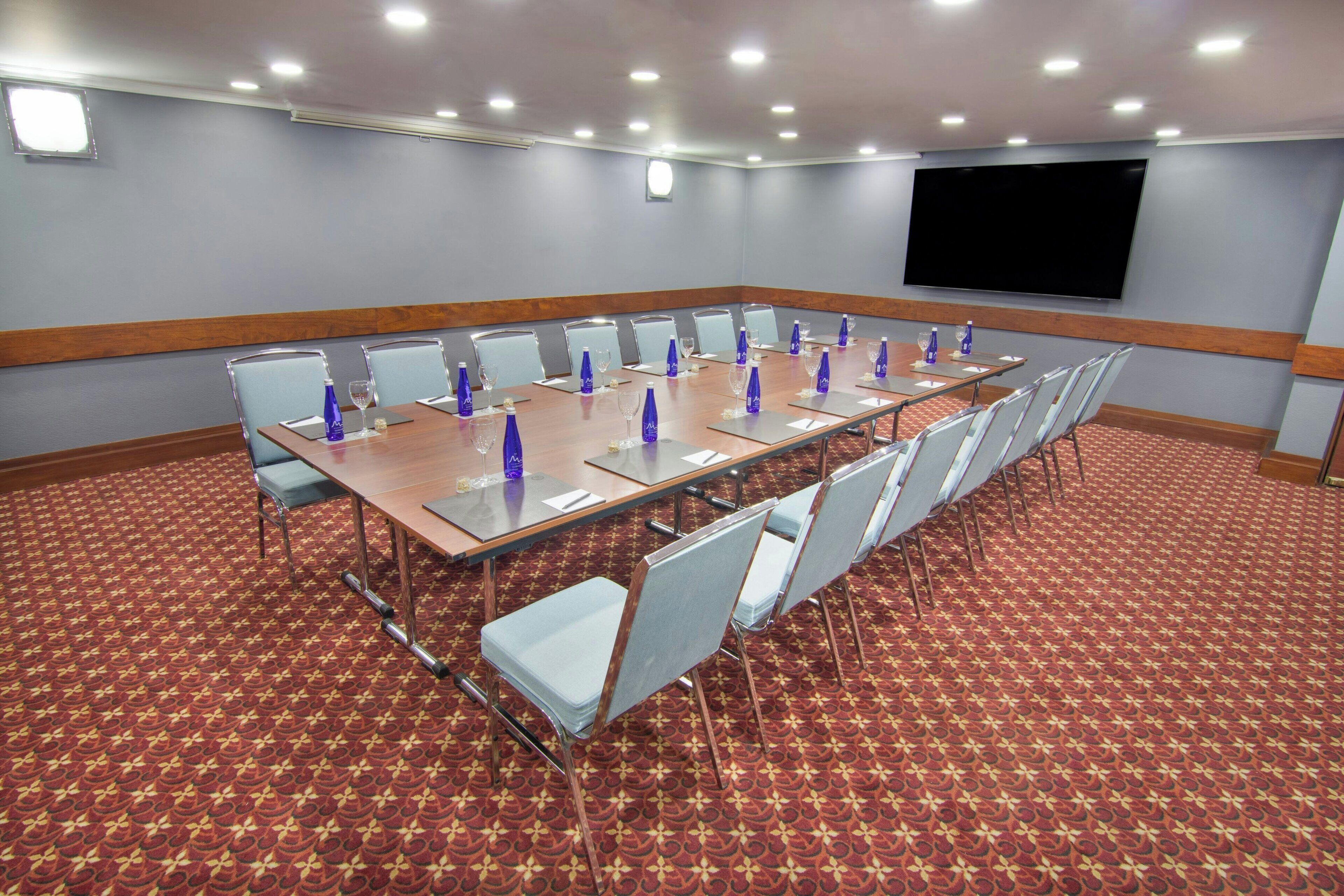 Une salle de conférence avec une longue table, des chaises et un téléviseur à écran plat fixé au mur.