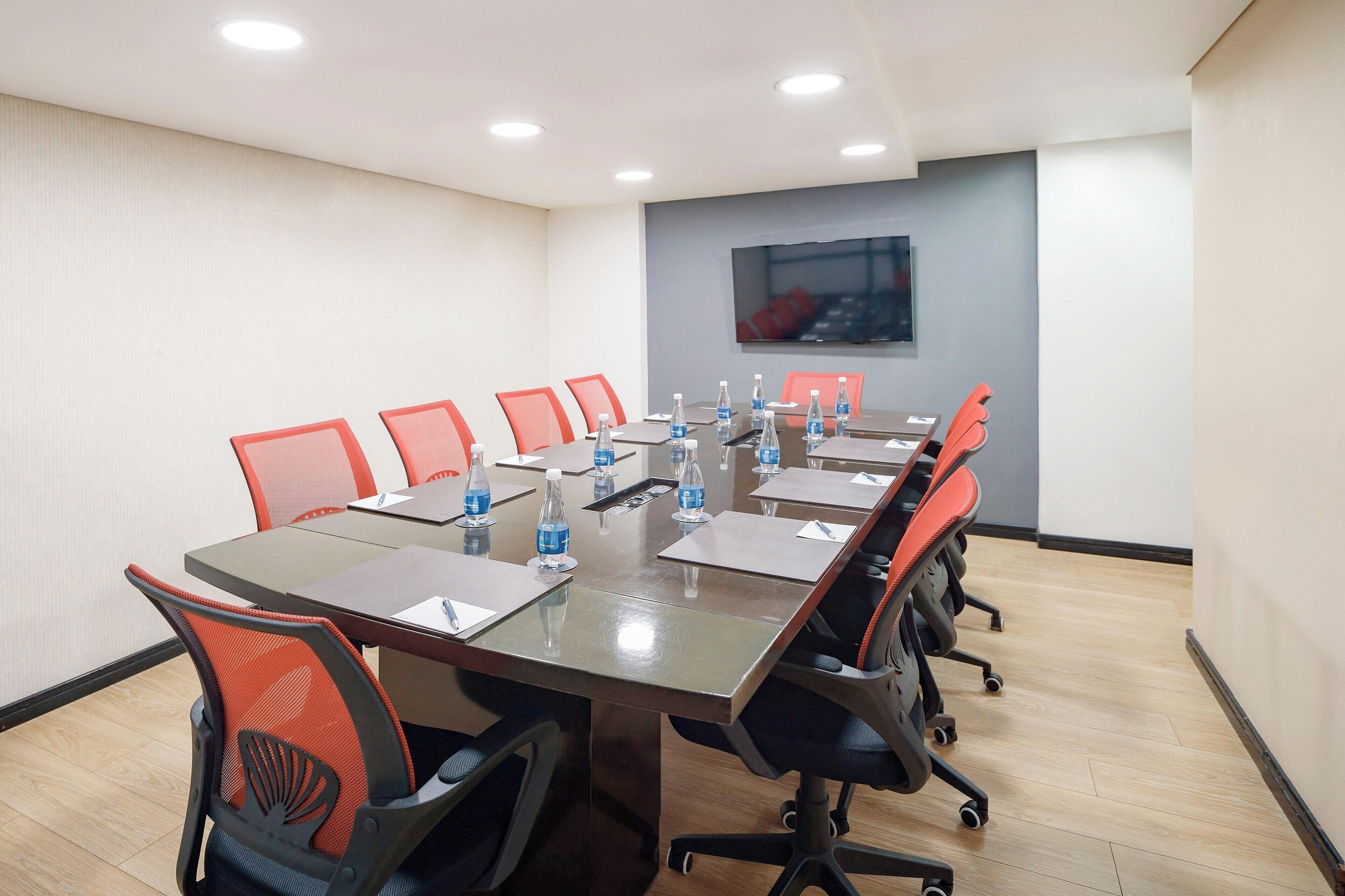 A conference room with a long table, red chairs, and water bottles.
