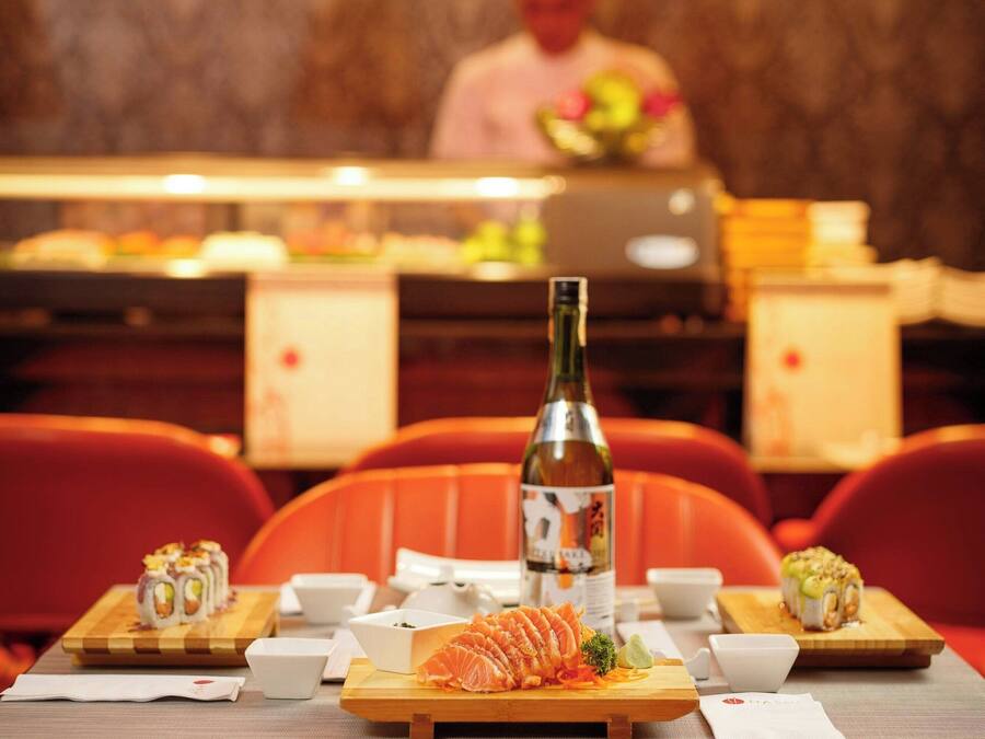 Entorn de restaurant amb un plat de sushi, una ampolla i un xef al fons.