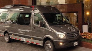A gray Sheraton van parked in front of a building with large windows and a brick facade.