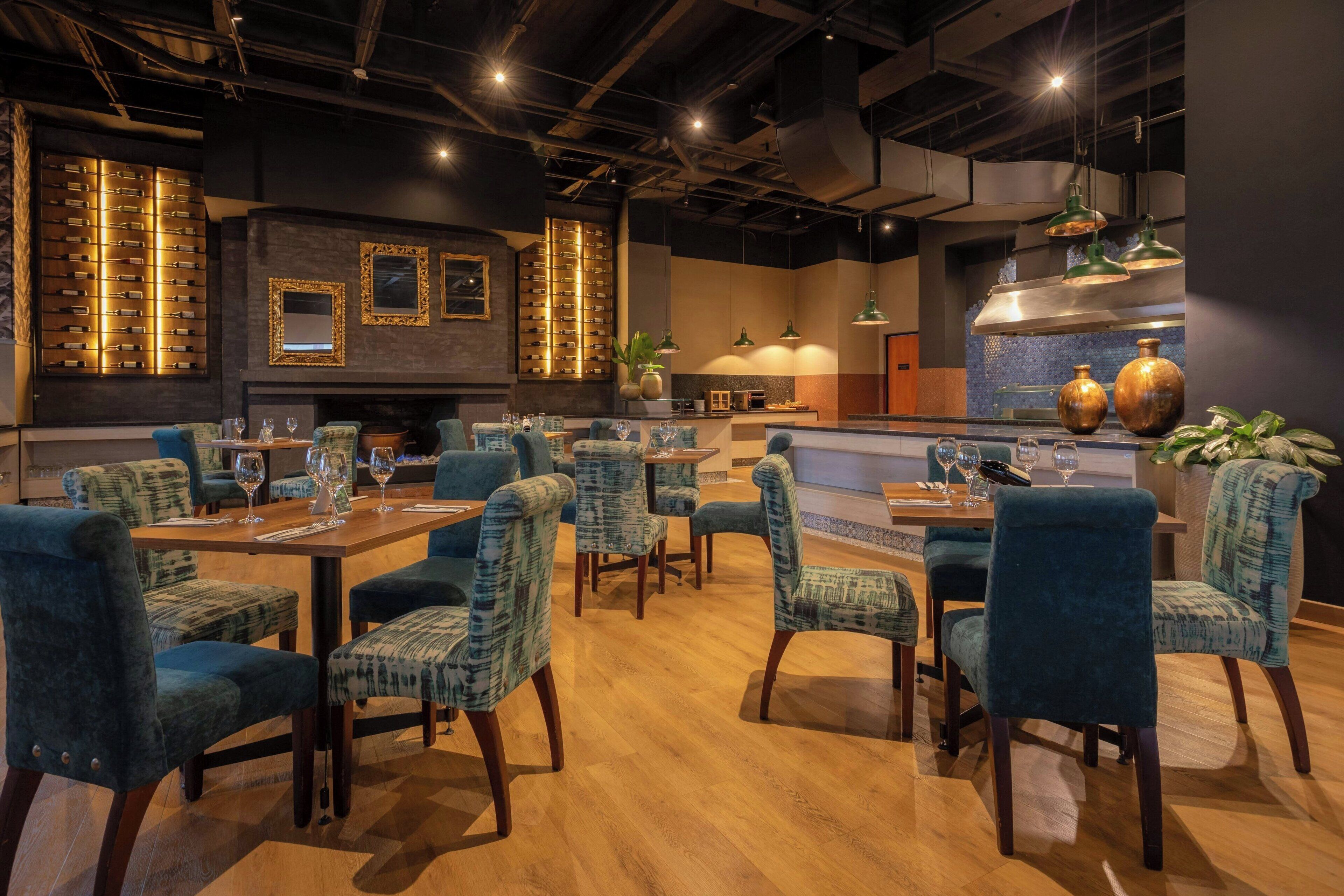 Un restaurant avec des tables en bois et des chaises à coussins bleus, un coin bar et des appliques murales décoratives.